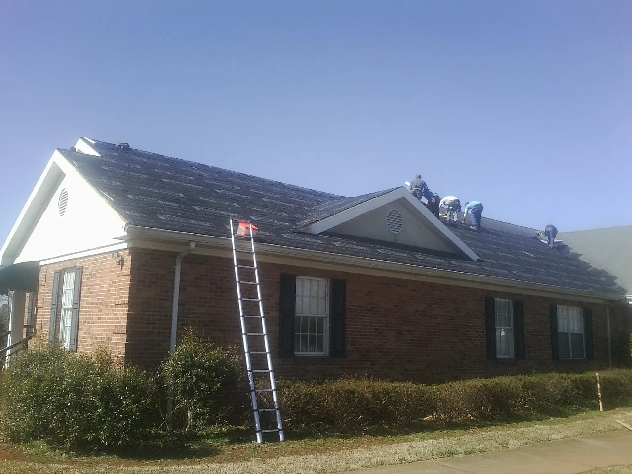 Crew tearing shingles off a brick ranch roof with a ladder set — Emergency Roof Repair work by our crew in Calder