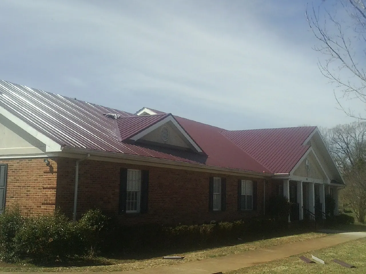 Red metal roof with gabled entries on a long brick building, from a Hail Damage Roof Repair job in Calder