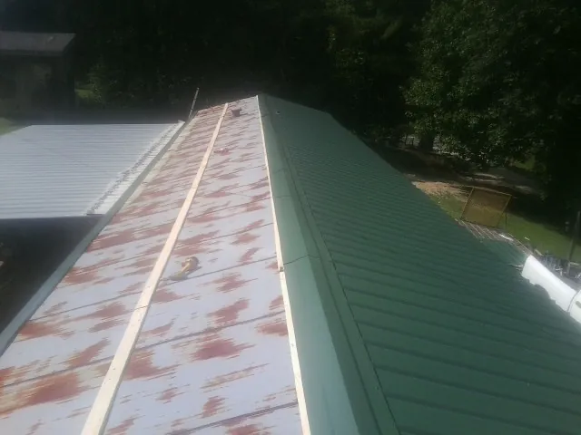Old rusted panels beside newly installed green metal roofing — Wind Damage Roof Repair by Roofing Brothers in Calder