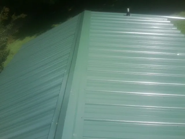 New green metal panels meeting at the ridge of a roof — Flat Roof Repair work by our crew in Calder