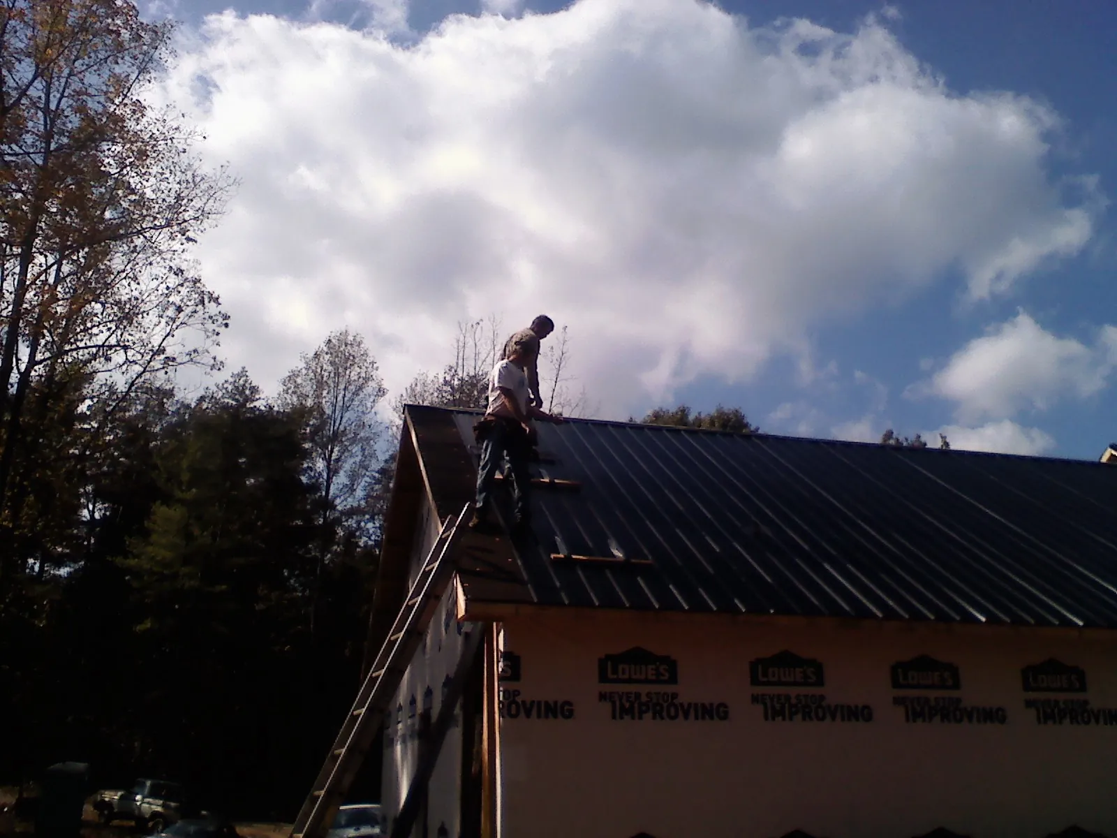 Roofer fastening dark metal panels high against a cloudy sky, from a Roof Inspection job in Calder