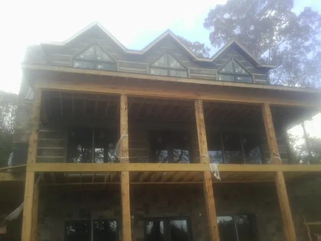 Dormers and porch framing on a large log home under construction — Roof Coating work by our crew in Calder