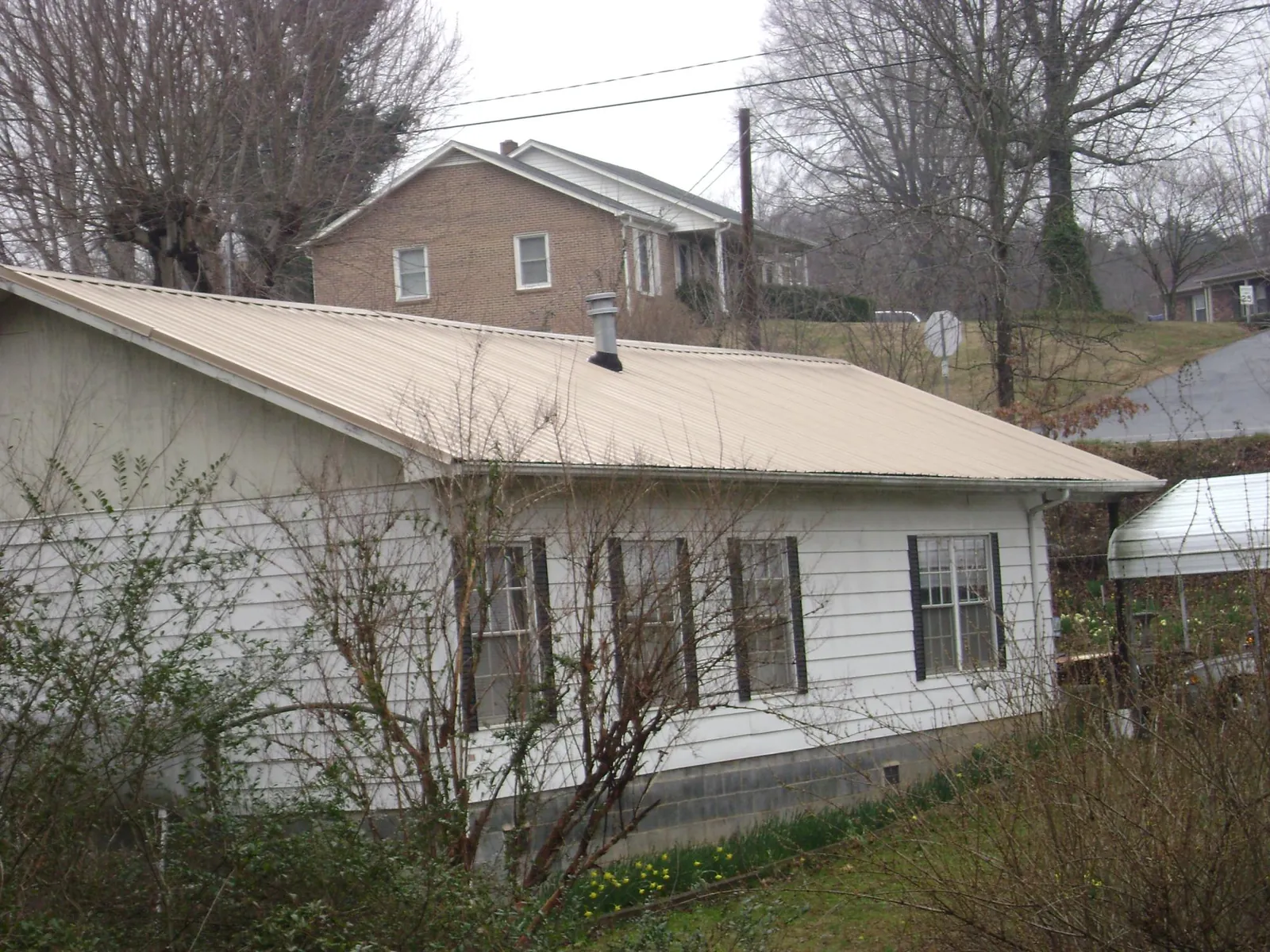 Tan metal roof on a white sided house set into a hillside — Commercial Roofing by Roofing Brothers in Calder
